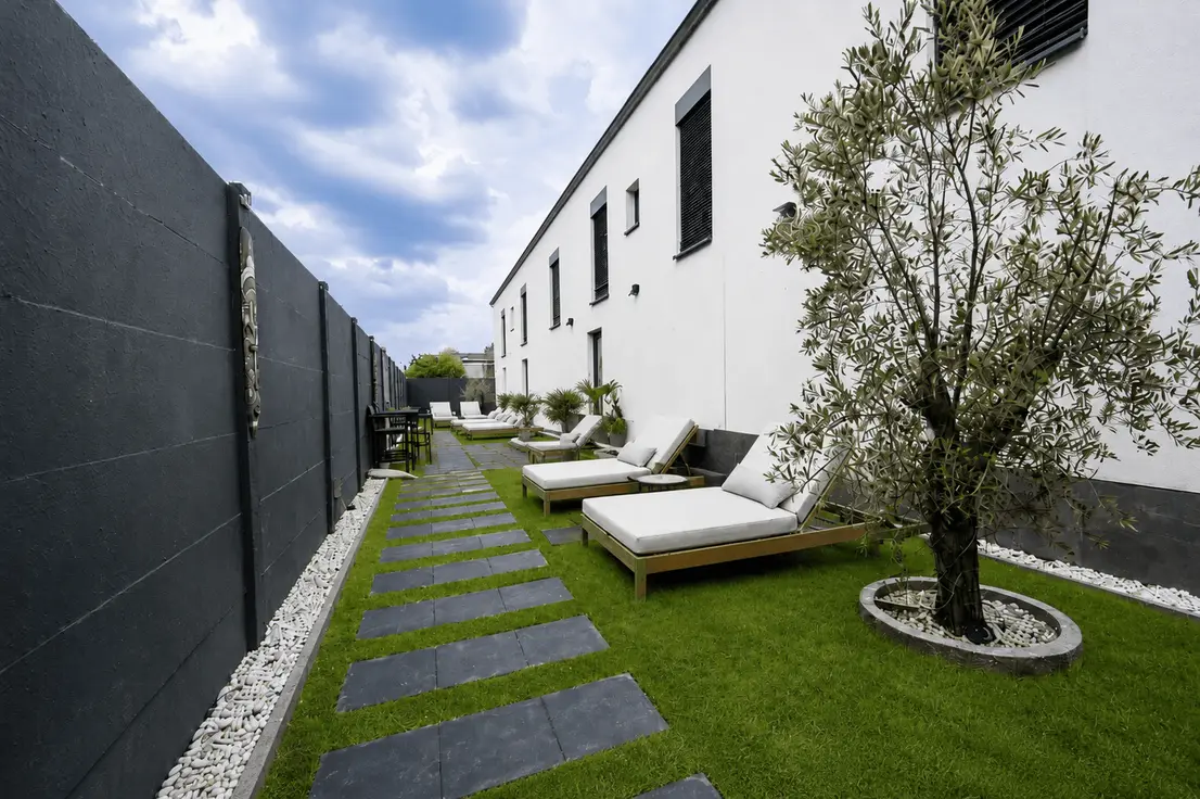 Privater Gartenbereich, der mit Liegestühlen, Rasen und einem Olivenbaum zum Verweilen einlädt